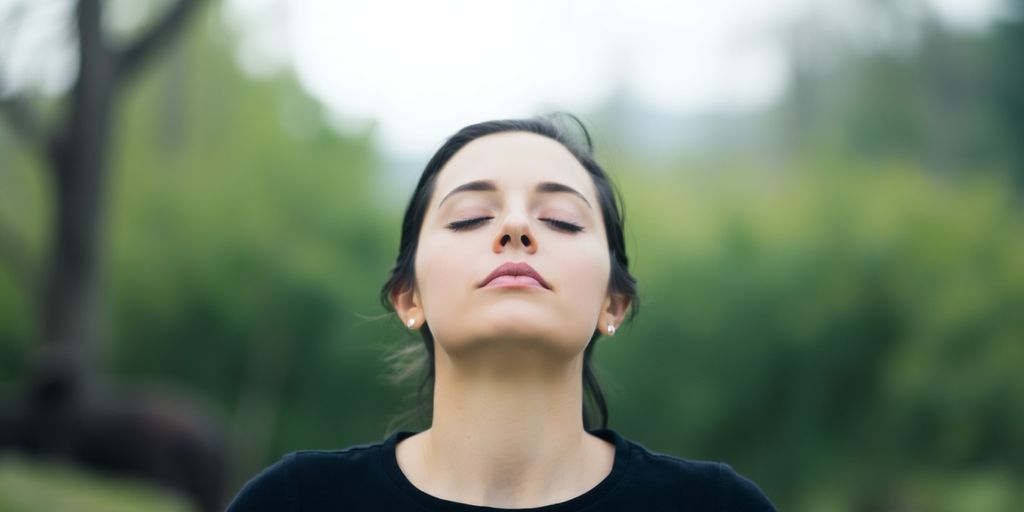 Person calmly breathing with eyes closed outdoors.